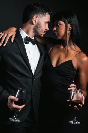 Stylish couple embracing while holding wine glasses, dressed in formal evening wear.